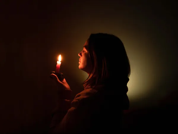 woman holding single candle in darkness